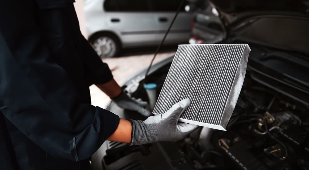 A mechanic holding an engine air filter over a car engine block.