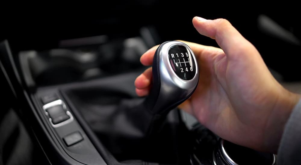 A hand is shown holding a shifter knob in a vehicle.