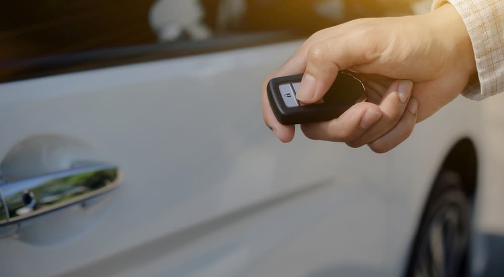 A person using a keyless remote to enter a white car.