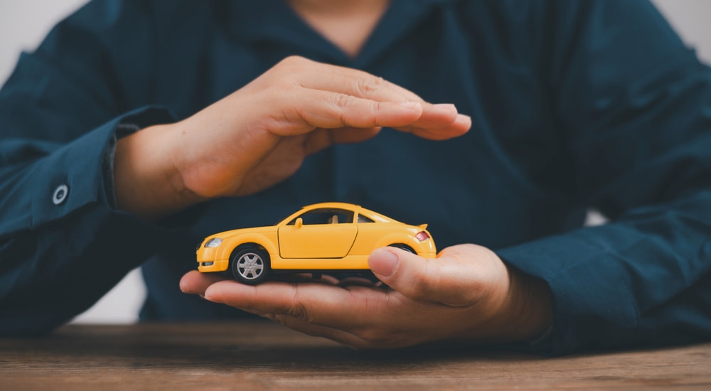 A person holding their hand over a yellow toy car.