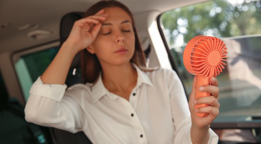 A person is shown holding a fan in a vehicle.