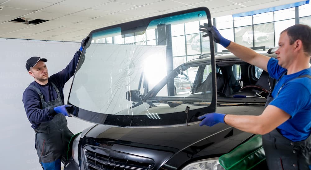 Two technicians are shown replacing a broken windshield.