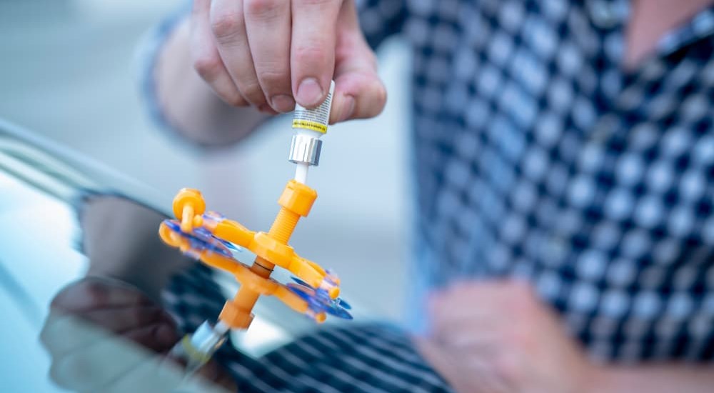 A person is shown using a windshield repair kit.