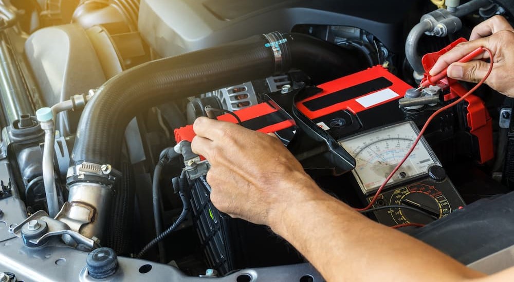 A mechanic is shown using a multimeter to test a battery.