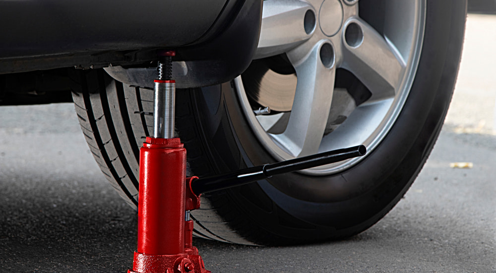 A red bottle jack lifting a car.