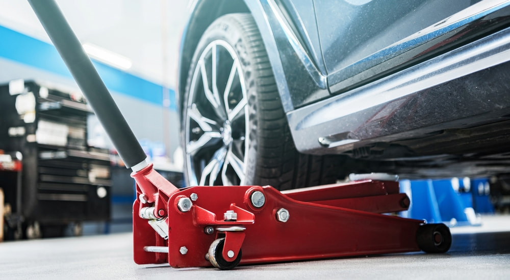 A red floor jack being used to lift a car.