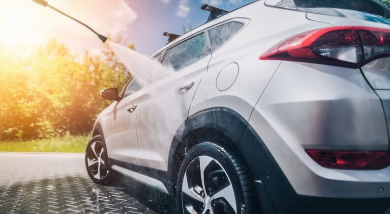 A hose is shown spraying a car on a sunny day.