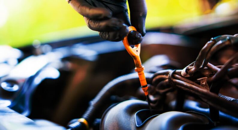 Close-up of a mechanic using a dipstick to check engine oil level.