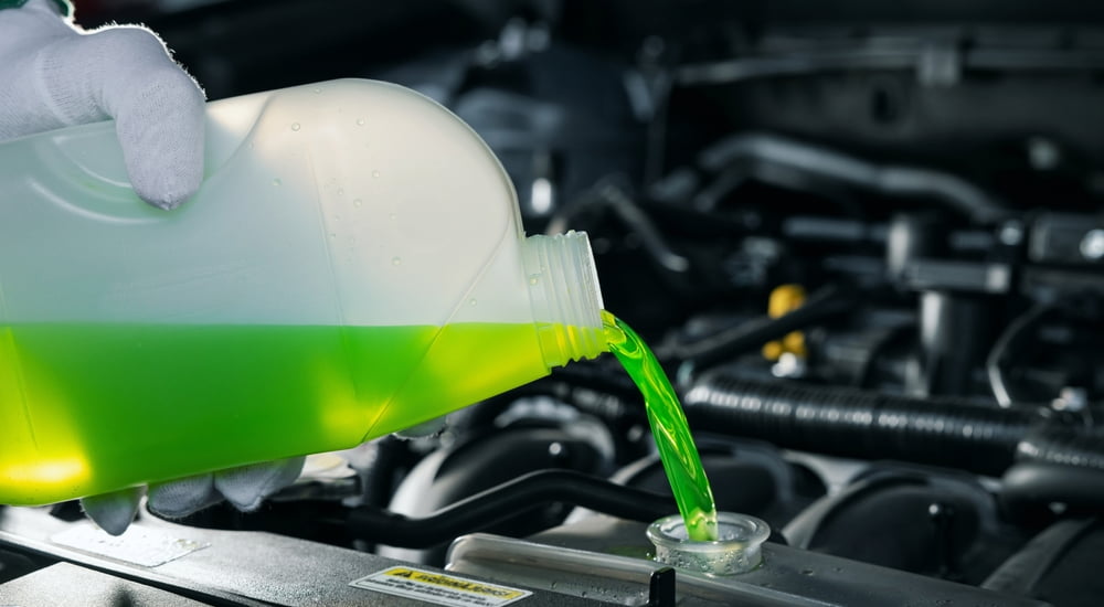 A can of coolant being poured into a radiator.