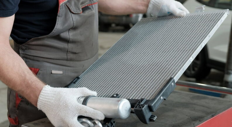 A mechanic holding a car radiator during a radiator repair.