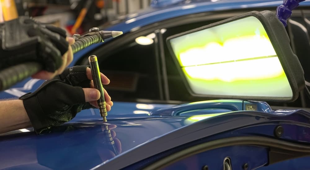 A mechanic performing a paintless dent repair on a blue car.