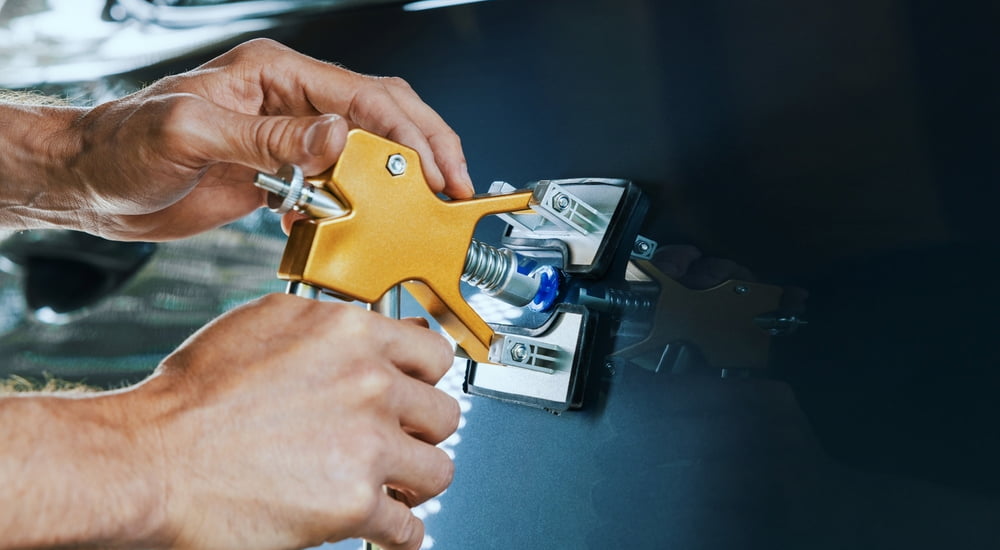 A mechanic performing a paintless dent repair on a black car.