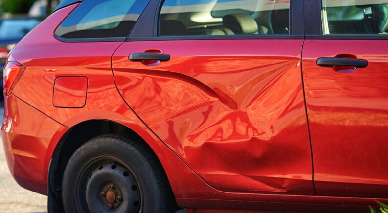 A large dent on the passenger side door of a red car.