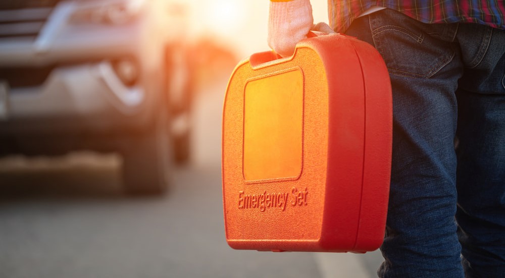 A person is shown holding an orange emergency roadside kit.