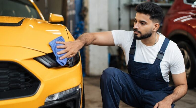 A technician is shown cleaning the headlight on a yellow vehicle.