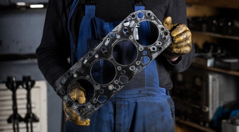 A mechanic is shown holding an old head gasket after performing a head gasket repair.