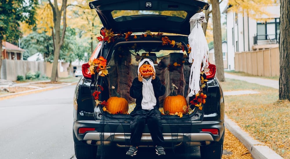 A child is shown wearing a costume near a decorated vehicle.