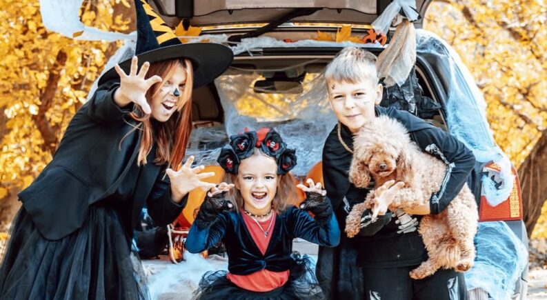 A family is shown wearing costumes near a decorated vehicle.