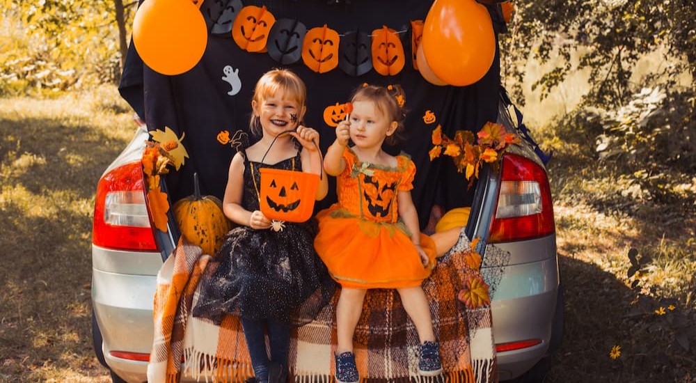 Two children are shown wearing costumes near a decorated vehicle.