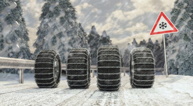 Four chained-tires are shown on snow near a sign.