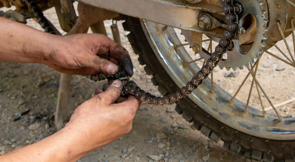 A person is shown fixing a broken motorcycle chain.