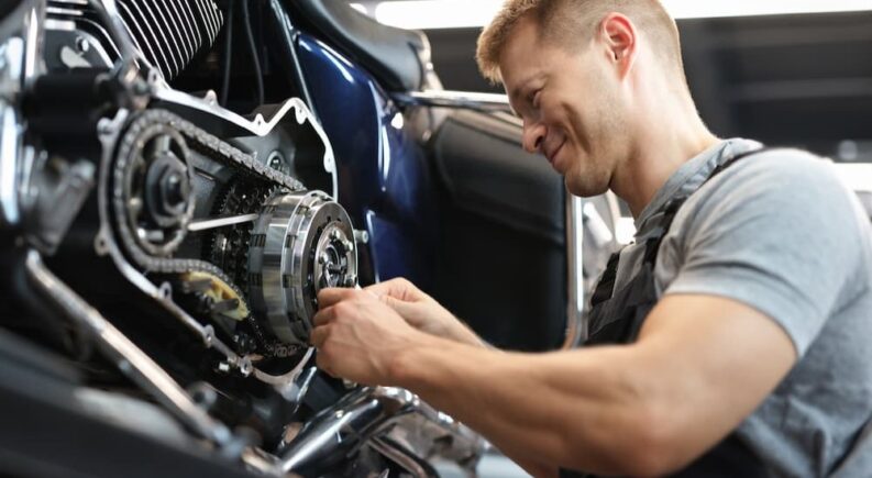 A mechanic is shown fixing a chain on a motorcycle.