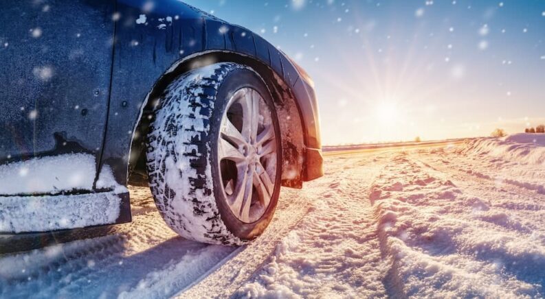 A close-up of a tire on a vehicle is shown parked on snow.