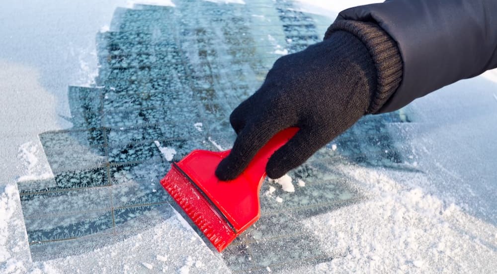 A person is shown using a window scraper on a frozen windshield.