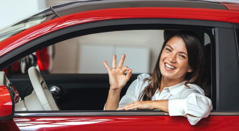 A person is shown sitting in a red car.