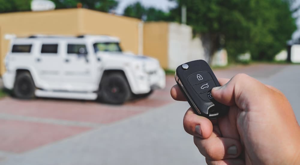 A person is shown holding a key fob near a white vehicle.