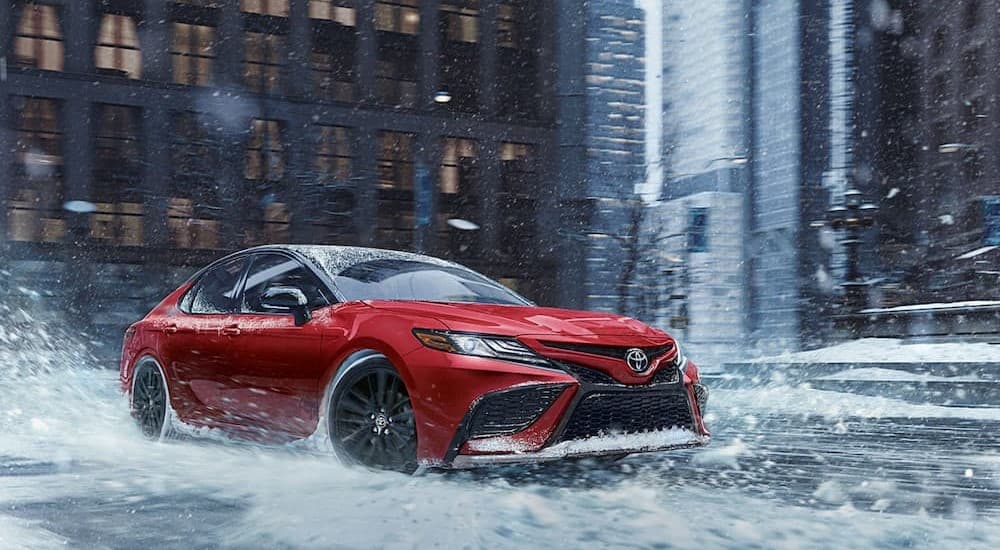 A red 2024 Toyota Camry driving through snow.