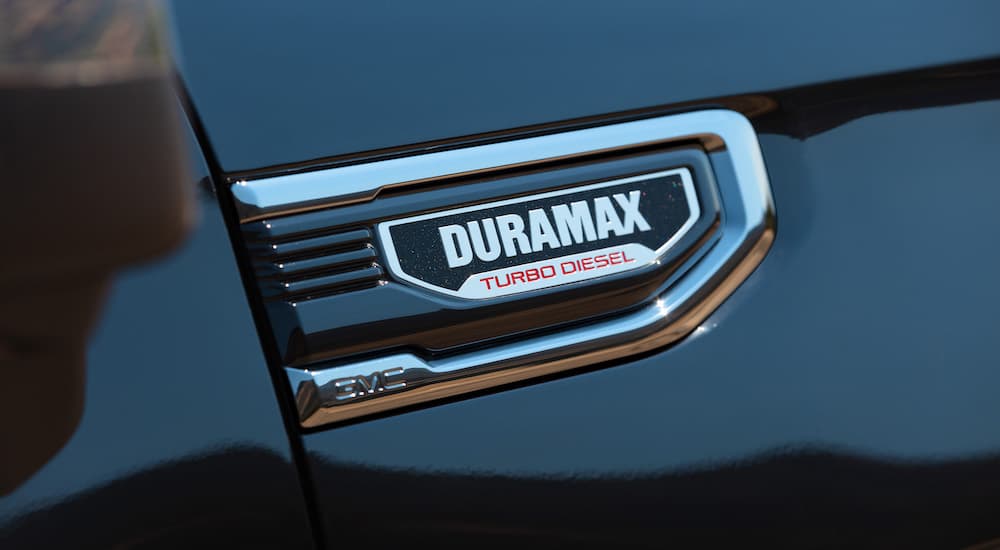 A close-up shows the Duramax badge on a blue 2024 GMC Sierra 1500.