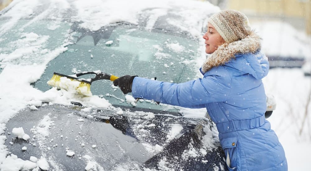 A person is shown cleaning snow off a vehicle.