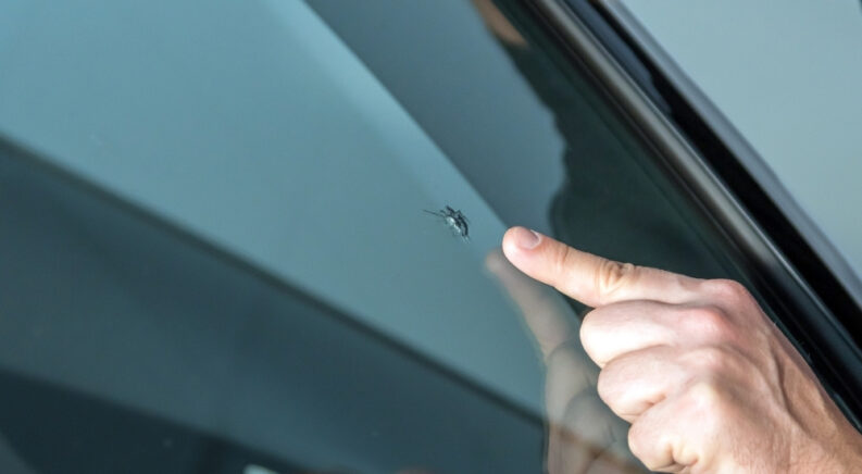 A hand is shown pointing to a windshield chip.