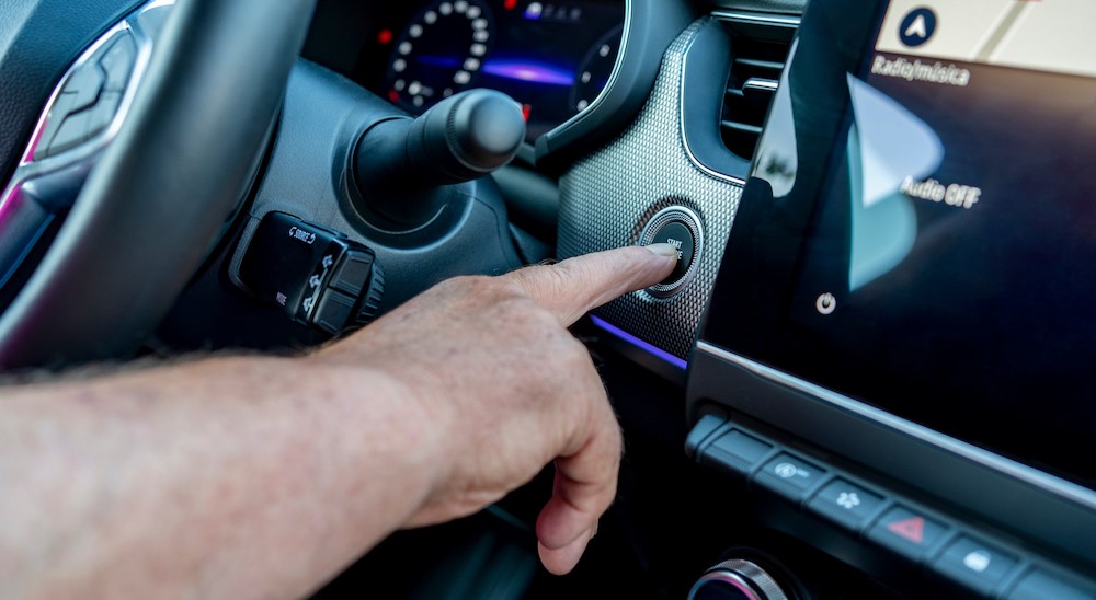 A finger pushing the "Auto Start/Stop Systems" button on the dashboard.