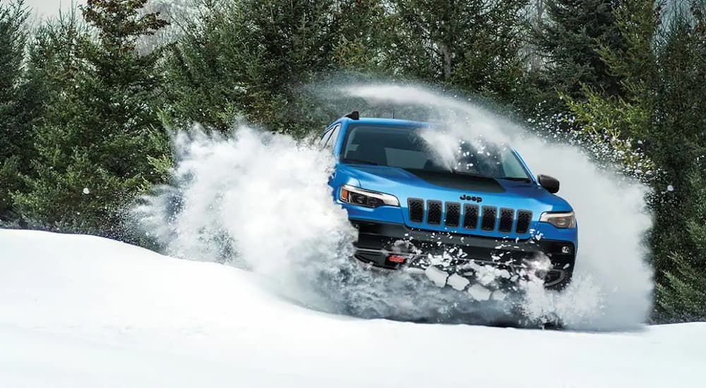 A blue 2026 Jeep Cherokee Trailhawk driving through snow.