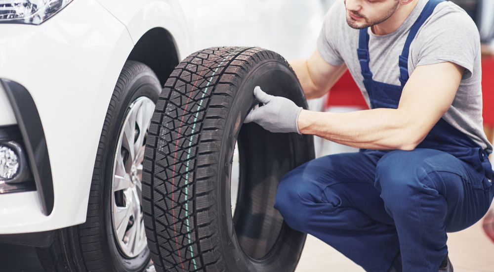 A mechanic replacing a winter tire on a white vehicle.