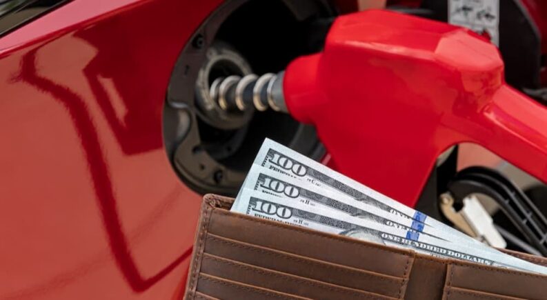 A wallet full of money near a gas pump.